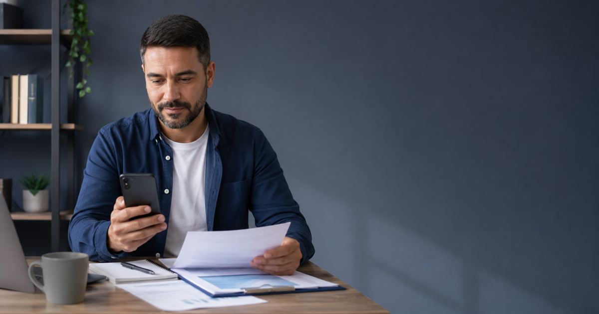 Trabalhador consultando o extrato do FGTS no celular e conferindo documentos financeiros